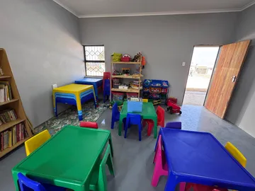 A brightly furnished room for the younger children, with colourful tables and chairs, toy shelves and a play mat.