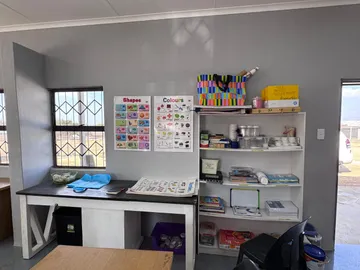 An art station with a long work bench, shapes and colours posters on the wall, and shelves of paints and materials.