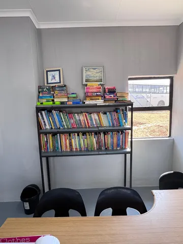 A metal shelf filled with children's readers, with dictionaries and reference books stacked on top.