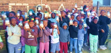 A large group of children outside the centre, each holding up their soup jar.