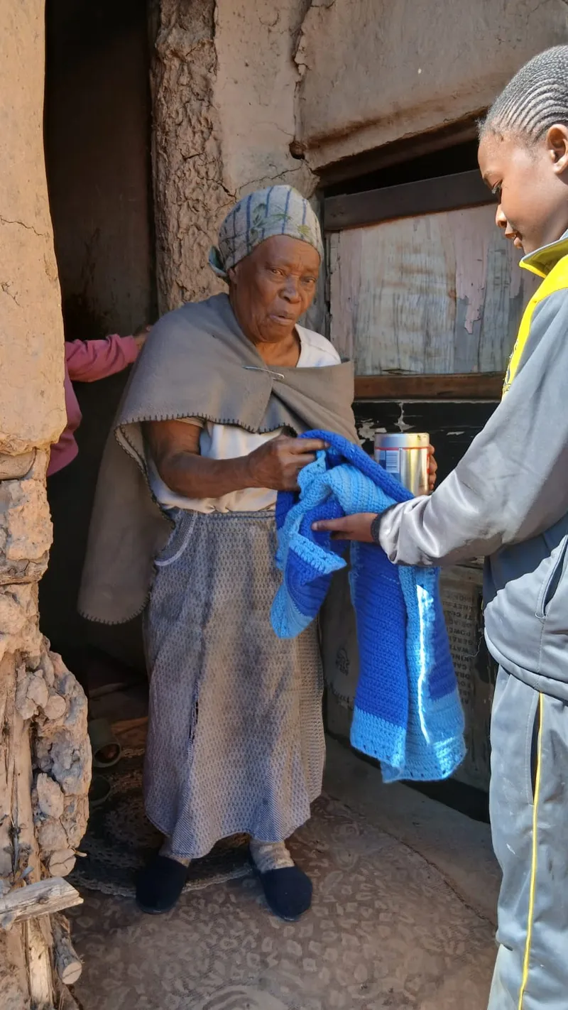 An elderly woman in her doorway receiving a blue knitted blanket from one of our youth.