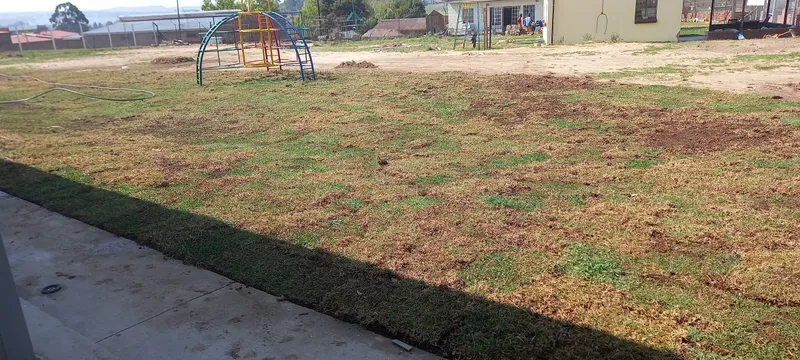 Freshly laid lawn running alongside the new building, with a climbing frame on the far side of the open ground.