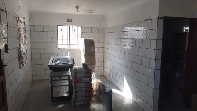 The new kitchen mid-installation, tiled floor to ceiling in white, with a steel sink and boxes of tiles still stacked on the floor.