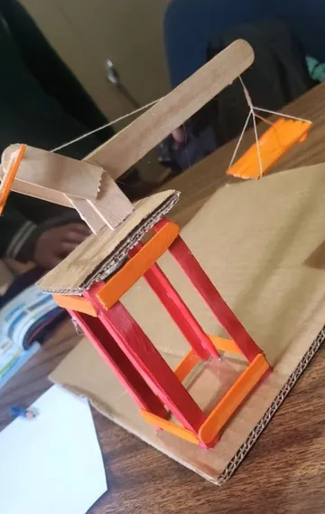 A painted model lever and pulley made from lolly sticks and string on a cardboard base.