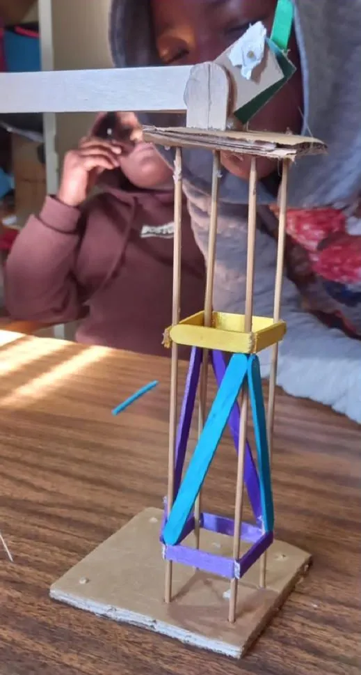 A model tower built from dowel, cardboard and painted lolly sticks, standing on a desk.