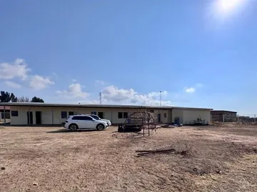 The full length of the new building seen from across the open ground, with a car parked outside.